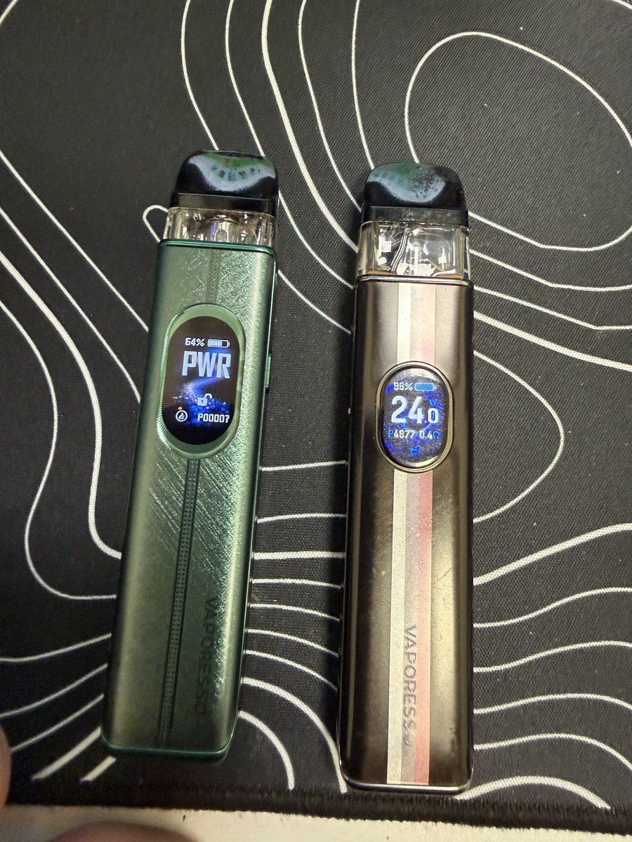 Vaporesso XROS 6 in Silk Green next to a Vaporesso XROS 5, both screens lit